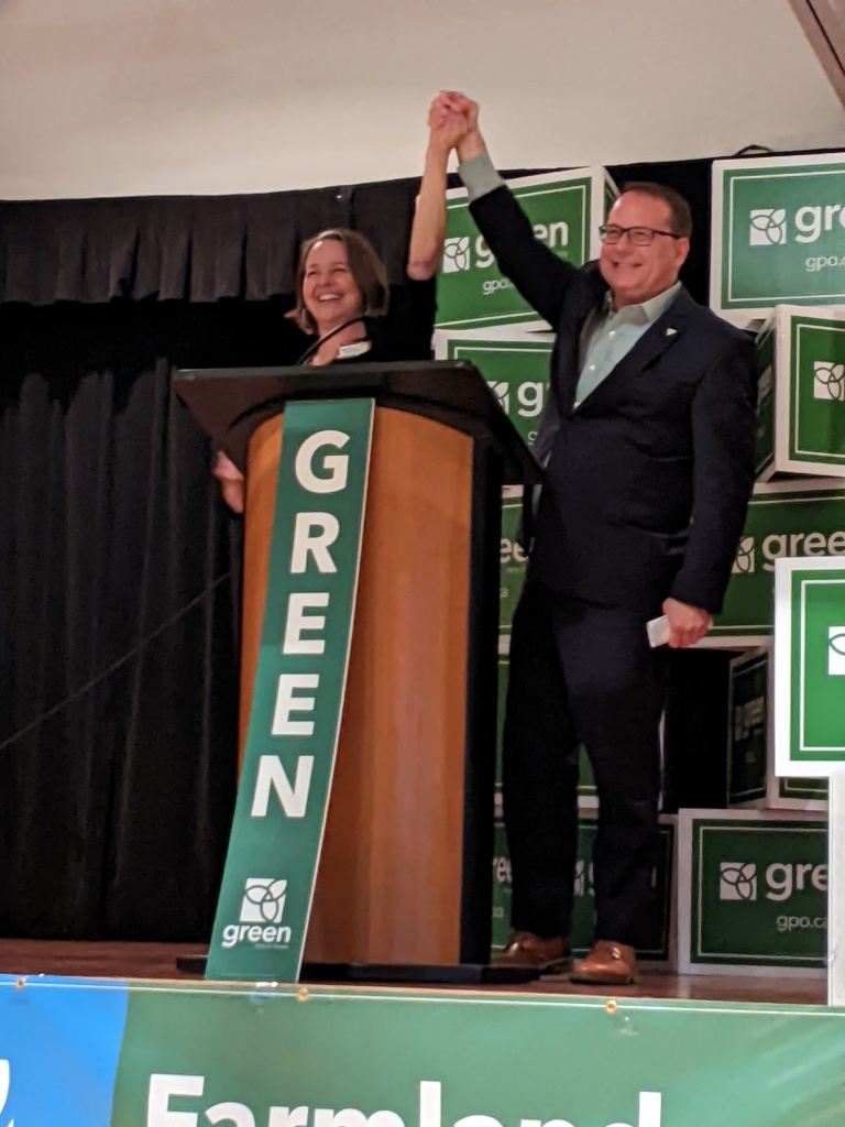 Mike Schreiner raises Aislinn Clancy's hand high amongst Green Party of Ontario signs.